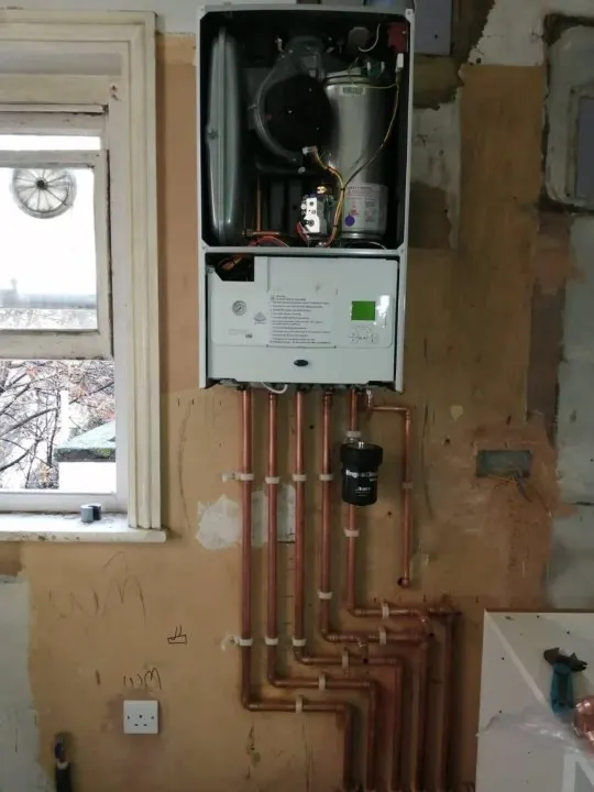 Wall-mounted boiler with several copper pipe runs and a magnetic filter in an unfinished wall